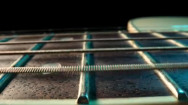Slider macro shot d'un cou de guitare acoustique avec cordes métalliques et des frettes sur fond noir. Les cordes de guitare classiques vibrent lors de la lecture de la chanson. Brun manche en bois d'une guitare extrême gros plan. — Video