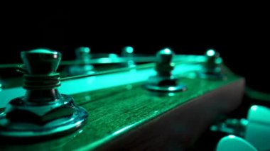 Ahşap gitar başlıkları, metal akort mandalları ve sicimle siyah arka planda yeşil ışıkla aydınlatılıyor. Gerginlik ve telleri ayarlamak için vidaları olan bir müzik aleti. Kapat..