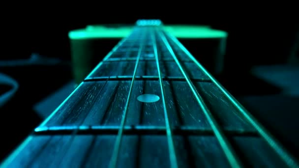 Kamera schwenkt über das Griffbrett einer klassischen Akustikgitarre vor schwarzem Hintergrund, angestrahlt von blauem Licht. Brauner hölzerner Gitarrenhals mit Metallsaiten und Bünden in extremer Nahaufnahme. — Stockvideo