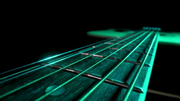 Camera pans over fretboard of classical acoustic guitar against black background, illuminated by green light. Brown wooden guitar neck with metal strings and frets extreme close up. — Stock Video