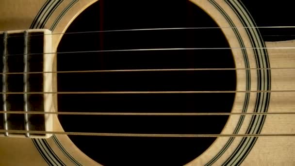 Part of body of a wooden acoustic guitar with a resonator sound hole and strings. Camera zooms into the sound hole and the screen turns black. Stringed musical instrument. Macro close up. — стоковое видео