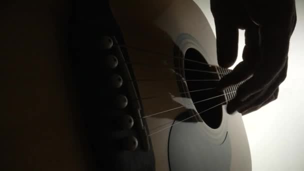 Low angle view of male guitarist playing wooden acoustic guitar on white background. Musicians hands touch strings. Strings of the guitar vibrate to reproduce musical melody of the song. Close up. — стоковое видео