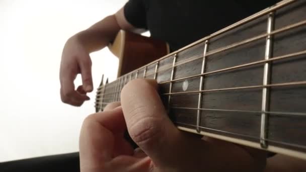 Músico tocando guitarra acústica sobre fondo blanco. Los dedos de los hombres tocan cuerdas de guitarra, haciendo que vibren y toquen la melodía de la canción. Detalles de madera diapasón guitarra y cuerdas de cerca. — Vídeo de stock