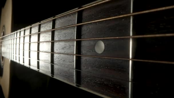 Kamera steker över fretboard av en klassisk akustisk gitarr mot en svart bakgrund. Brun gitarrhals i trä med metallsträngar och band extrem närbild. — Stockvideo