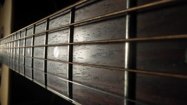 Kamera steker över fretboard av en klassisk akustisk gitarr mot en svart bakgrund. Brun gitarrhals i trä med metallsträngar och band extrem närbild. — Stockvideo
