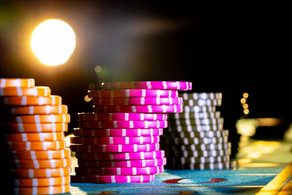 Conjunto de fichas coloridas para jogar no cassino em um fundo preto. Fichas de jogo amarelas e rosa na mesa de poker no escuro com luz de fundo. Fichas de poker para apostar de perto. — Fotografia de Stock