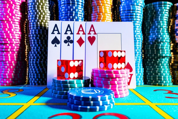 カジノの青いゲームテーブルの上の色のポーカーチップのセットを背景に4つのエースのクワッド。トランプ、異なる宗派のポーカーチップと2つの6つのクローズアップと赤いサイコロ. — ストック写真