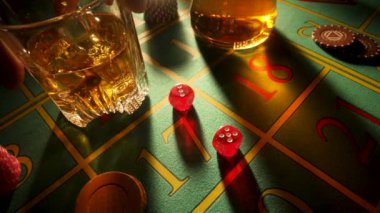 Bir adamın eli kumarhane masasına bir bardak viski koyar ve üç bayandan oluşan bir set hazırlar. İçki, kumar, zar ve kumarhane fişleri olan karanlık bir poker masasını kapatın..