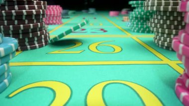 Kamera yeşil oyun masasında siyah arka planda yığınla kumarhane fişi gösteriyor. Chip yavaş çekimde masanın üzerine düşüyor. Kumarhanede rulet ya da poker oynamak için masa.