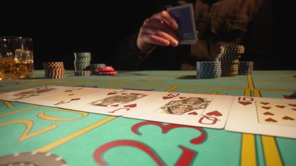 Joueur risqué dans le casino regarde et plie les cartes. L'homme boit du whisky assis à la table de jeu pour jouer au poker. Les jetons de casino sur la table de jeu verte ferment. Concept de divertissement et style de vie de luxe. — Video