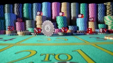 Kumarhane fişleri ve kırmızı zarlar yeşil kumarhane masasında siyah bir zemine karşı. Bir çip masada döner ve yavaş çekimde yakınlaşır. Rulet, poker, barbut, blackjack.