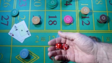 Kumarhanedeki yeşil rulet masasının arka planına karşı ağır çekimde kırmızı zarları atan bir erkek. Kumarbaz, kumarbaz, barbut, poker. Kumarhane fişleri ve kartları kumar masasının üzerine serilir..