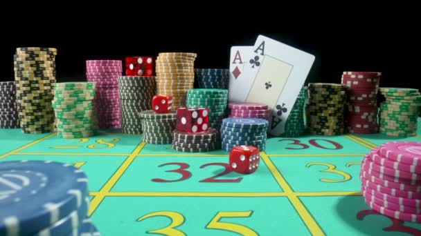 Set chip berwarna-warni, bermain kartu dan dadu merah di meja judi di kasino. Dadu jatuh di atas meja Menutup dalam gerakan lambat. Poker ditata pada latar belakang hitam. — Stok Video