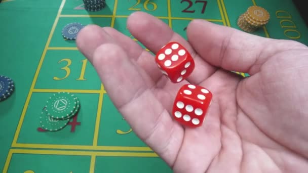 Male hand shakes red dice in slow motion against the background of a green roulette table in a casino. Man gambler, gambling, craps, poker. Casino chips are laid out on the gaming table close up. — Stock Video