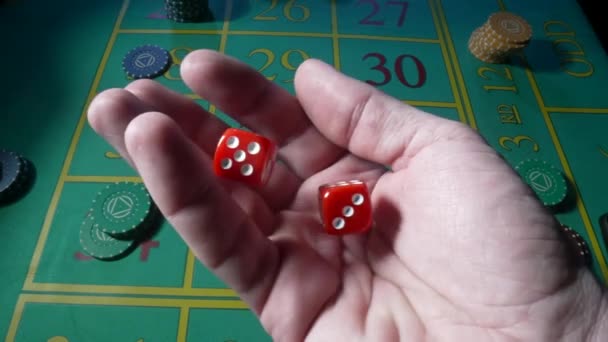 La main masculine serre des dés rouges au ralenti sur fond de table de roulette verte dans un casino. Homme joueur, jeu, craps, poker. Les jetons de casino sont disposés sur la table de jeu close up. — Video