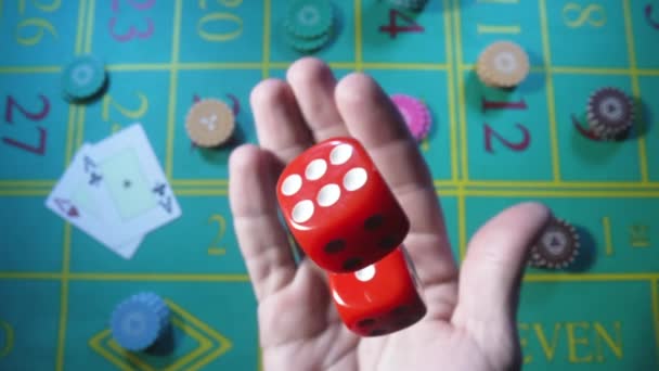 Male hand tossing up red dice in slow motion against background of green roulette table in casino. Man gambler, gambling, craps, poker. Casino chips and cards are laid out on gaming table close up. Лицензионные Стоковые Видеоролики