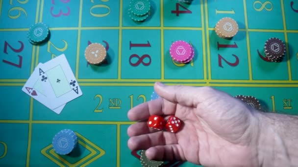 Male hand tossing up red dice in slow motion against background of green roulette table in casino. Man gambler, gambling, craps, poker. Casino chips and cards are laid out on gaming table close up. — стоковое видео