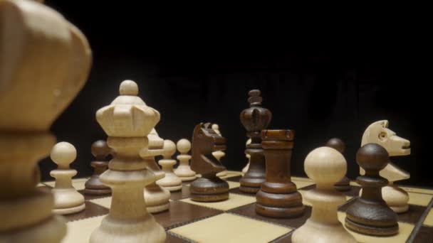 Camera pans over chessboard with chess pieces placed and focuses on brown horse. White and brown wooden chess set on squared board on black background. Wooden figures for playing chess close up. — Stockvideo