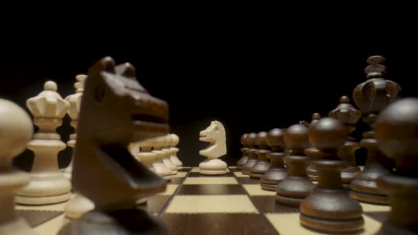 İzole edilmiş siyah bir zemine satranç taşları yerleştirilmiş satranç tahtası. Kare tahtada beyaz ve kahverengi ahşap satranç takımı. Satranç oynamak için ahşap figürler. Entelektüel oyun, düşünme stratejisi. — Stok video