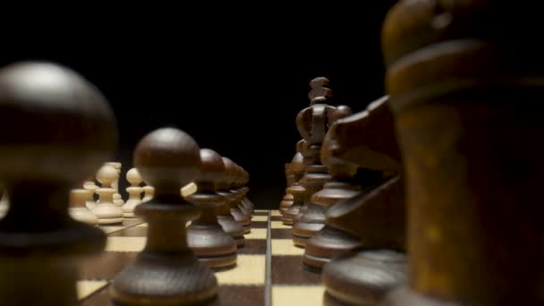 Chessboard with chess pieces placed on isolated black background. White and brown wooden chess set on squared board. Wooden figures for playing chess. Pawn, king, queen, horse, rook, bishop close up. — Stockvideo