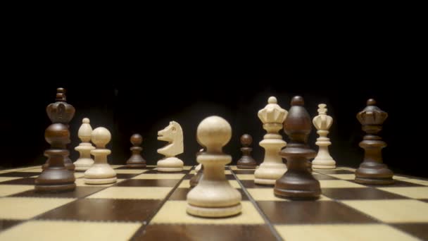 Chessboard med schackpjäser placerade på isolerad svart bakgrund. Vit och brun träschack på fyrkantig bräda. Träfigurer för att spela schack. Pant, kung, drottning, häst, torn, biskop på nära håll. — Stockvideo