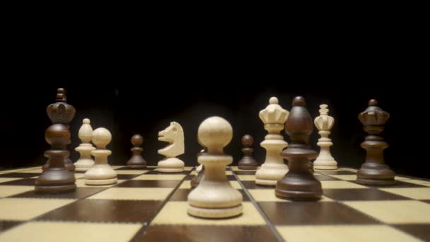 Chessboard with chess pieces placed on isolated black background. White and brown wooden chess set on squared board. Wooden figures for playing chess. Pawn, king, queen, horse, rook, bishop close up. — стоковое видео