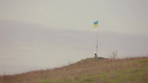 En ensam flicka sitter på en kulle under ukrainsk flagg. — Stockvideo