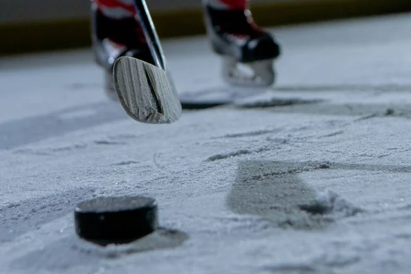 Hockey in der Eisarena. Der Moment, in dem man den Puck mit dem Stock trifft. Ein Athlet verfeinert seine Fähigkeiten beim Eishockeyspielen auf dem Eis eines Stadions im Dunkeln mit Gegenlicht. Beine aus nächster Nähe. — Stockfoto