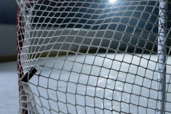 冰球击中了网,进了一个球.冰球飞入网中的特写.射门宽。从网络后面看。带有聚光灯的黑暗曲棍球竞技场. — 图库照片
