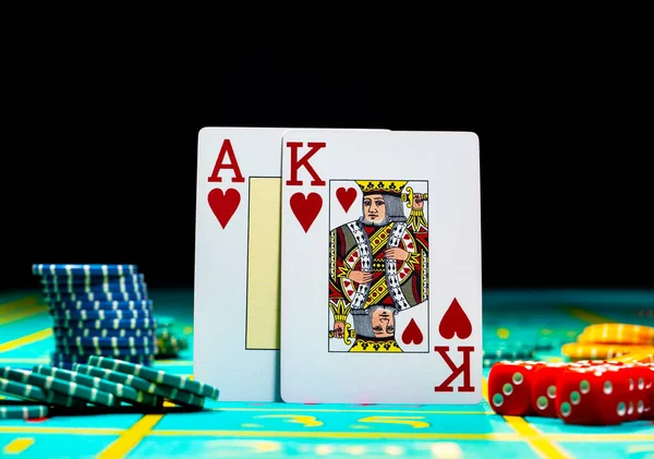 A pair of king and ace of hearts of playing cards on green gaming table in a casino. Close up of playing cards, chips and dice for gambling on black background. Set for poker. Gambling in the casino. — Stock Photo, Image