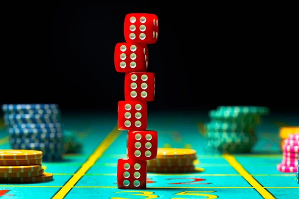 Six red dice are stacked on a gaming table in a casino. Dice for poker or craps and casino chips on black background close up. The concept of gambling, betting and money.