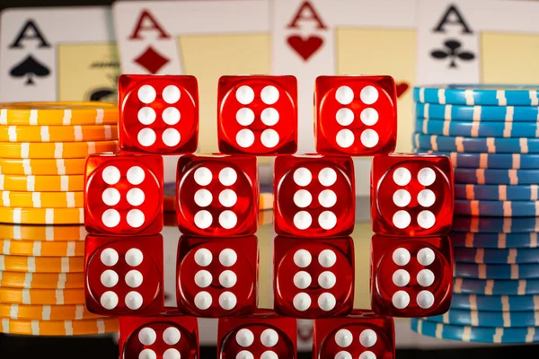 A set of red dice and blue yellow casino chips on the background of four of a kind of four aces on gaming table in casino. Playing cards, poker chips of different denominations and red dice close up.