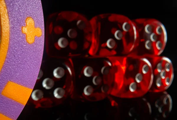 A set of red dice next to a casino chip on a black background. Close-up of dice for poker and craps. The concept of gambling, betting, money and success. Стоковое Фото