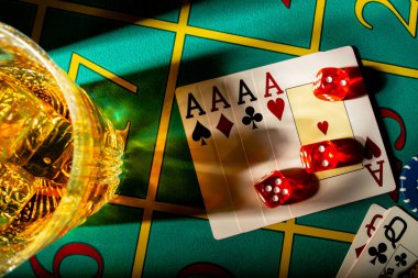 Top view of table in casino with glass of whiskey and set of four aces. Close up of a dark gambling table with booze, cards, dice and casino chips. The concept of gambling or poker and entertainment.