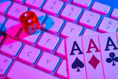 Computer keyboard and quads of four aces, illuminated with pink light on black background. Cards, casino chips and dice close up. Concept of gambling, online betting in casino. Online gambling. clipart