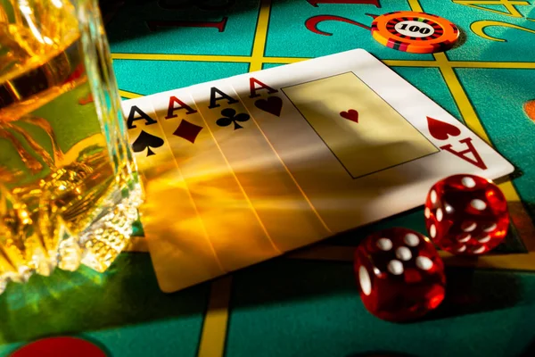Gaming table in casino with glass of whiskey and set of four aces. Close up of a dark gambling poker table with booze, cards, dice and casino chips. The concept of gambling or poker and entertainment. — Photo