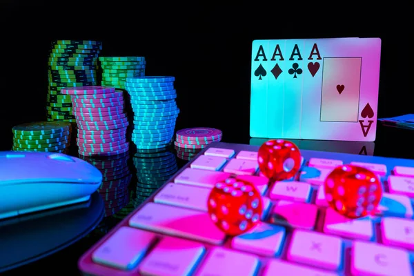 Computer keyboard and quads of four aces, illuminated with pink light on black background. Cards, casino chips and dice close up. Concept of gambling, online betting in casino. Online gambling.