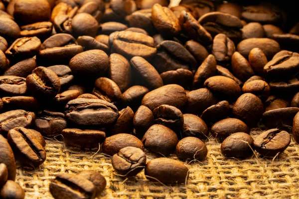 Dark brown roasted coffee beans lying on burlap. Organic coffee seeds close up. Food and drink background for cafe and cafeteria. Grains for the preparation of an invigorating and strong morning drink — 스톡 사진