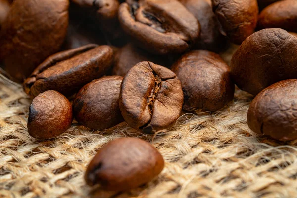 Dark brown roasted coffee beans lying on burlap. Organic coffee seeds close up. Food and drink background for cafe and cafeteria. Grains for the preparation of an invigorating and strong morning drink — 스톡 사진