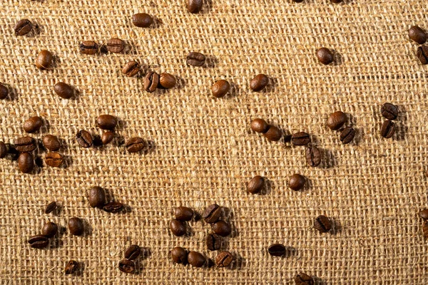 Top view of brown roasted coffee beans on burlap cloth. Coffee seeds laid out on a textured fabric with interlaced fibers. Food and drink background. Aromatic beans of Robusta or Aribica. Close up. — 스톡 사진