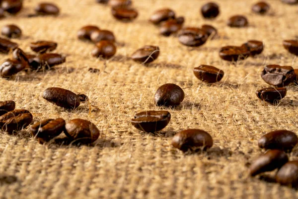 Brown freshly roasted coffee beans on burlap cloth. Coffee seeds laid out on a textured fabric with interlaced fibers. Food and drink background. Aromatic beans of Robusta or Aribica. Close up. — 스톡 사진