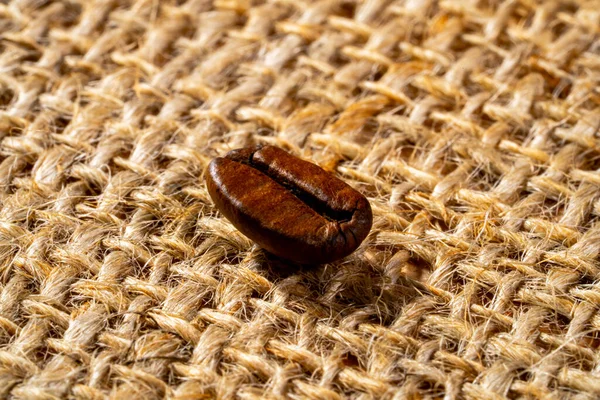 Brown freshly roasted coffee bean on burlap cloth. Coffee seed laid out on a textured fabric with interlaced fibers. Food and drink background. Aromatic bean of Robusta or Aribica. Close up. — 스톡 사진