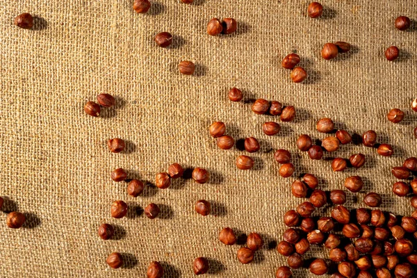 Brown peeled hazelnuts on a burlap cloth. Top view of round nuts close up. Hazel seed laid out on a textured fabric with interlaced fibers. Dry hazel, healthy nuts, nutritious snack. — kuvapankkivalokuva