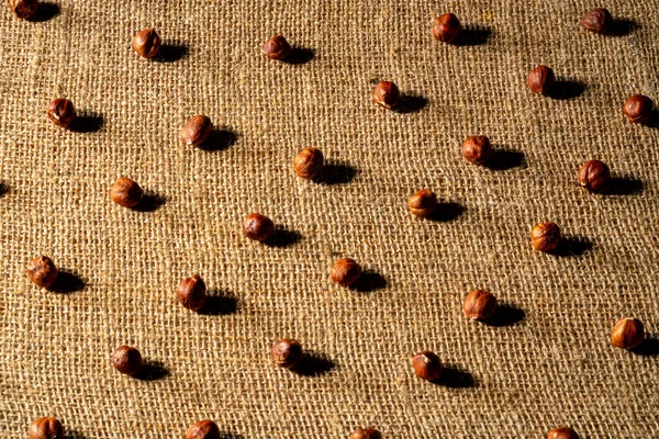 Brown peeled hazelnuts on a burlap cloth. Top view of round nuts close up. Hazel seed laid out in rows on a textured fabric with interlaced fibers. Dry hazel, healthy nuts, nutritious snack. — kuvapankkivalokuva