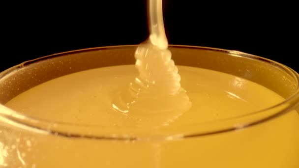 A trickle of thick golden honey flowing into a glass. Close up macro shot of honeyed molasses dripping on isolated black background. Sweet dessert. Background of organic and curative food. — Vídeo de Stock