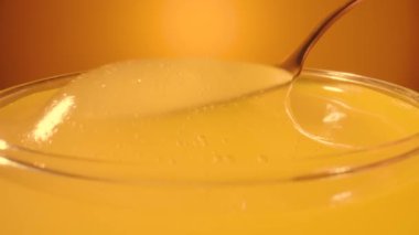 Bal damlıyor, kaşıktan bardağa dökülüyor. Kalın bal pekmezi dolu bardağa damlıyor. Altın bal sıvısına yakın, arıcılığın tatlı ürünü. Sarı arkaplana şeker şurubu dökülüyor.