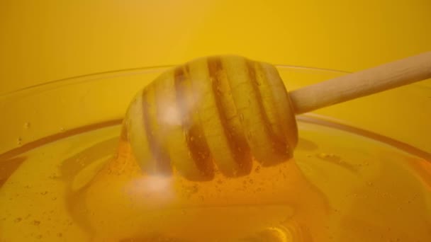 Miel goteando, vertiendo de un recipiente de miel en un recipiente de vidrio. Miel gruesa orgánica saludable que se sumerge de una cuchara de miel de madera, de cerca. Líquido dorado, melaza dulce, jarabe de azúcar. Producto biológico de abeja. — Vídeo de stock