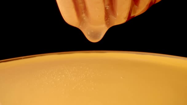 Honey dripping, pouring from a honey dipper on a black isolated background. Healthy organic thick honey dipping from a wooden honey spoon, close up. Golden liquid, sweet molasses, sugar syrup. — Vídeo de stock