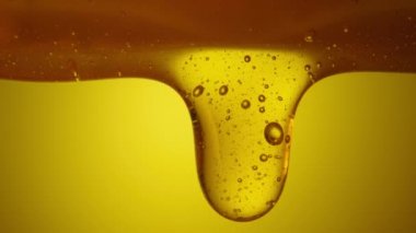 Drops of thick golden honey flowing down on a yellow background. Close up of sweet nectar or molasses being spilled. Liquid honey pours and drips. Sugar syrup is pouring. Healthy and curative dessert.