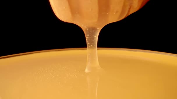 Miel goteando, vertiendo de un cazo de miel sobre un fondo negro aislado. Miel gruesa orgánica saludable que se sumerge de una cuchara de miel de madera, de cerca. Líquido dorado, melaza dulce, jarabe de azúcar. — Vídeo de stock